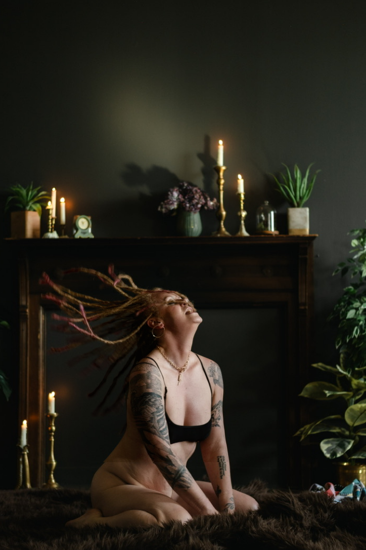 Marta Kagan kneeling nude in candlelight, hair flying, wearing a black bralette